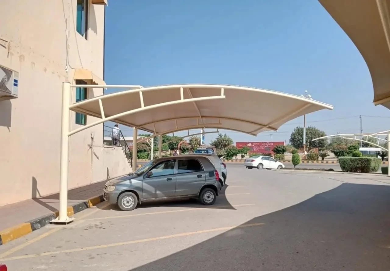 Curved tensile car parking shade beside a building, with open vehicle access beneath